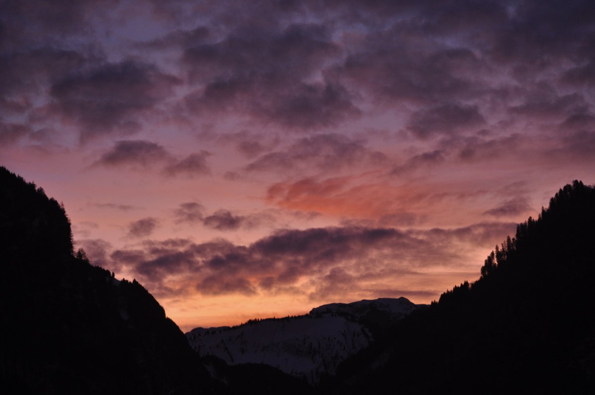 Unten ist ein schwarzer Horizont mit links und rechst einem Bergabhang. Das Morgenrot ist unten ein leicht gelbliches Rot. Gegen oben wird es Rot, und zuoberst ist es rot-violett. Es ist gespickt mit mehr ode weniger Wolken, die gräulich sind. Eine ist kräftig Rosa.